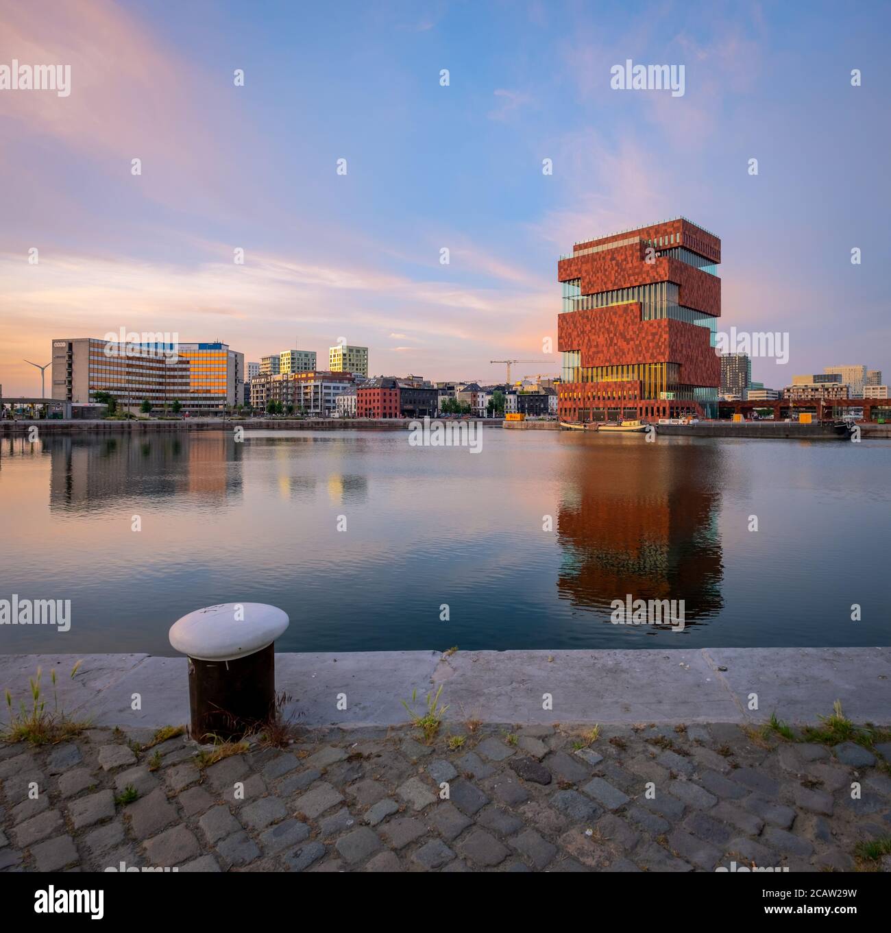The landmark MAS museum reflected in the Bonaparte dock in the Northern part of the city of Antwerp. Old metal bollard in the foreground Stock Photo