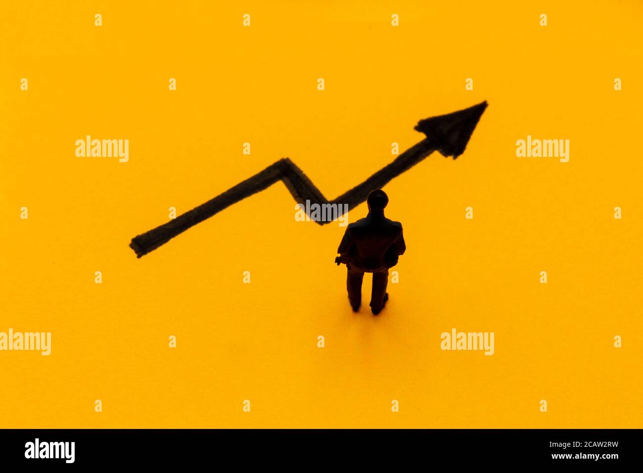 Miniature figurine posed as businessman in front of ascending graph arrow, positive performance concept image Stock Photo