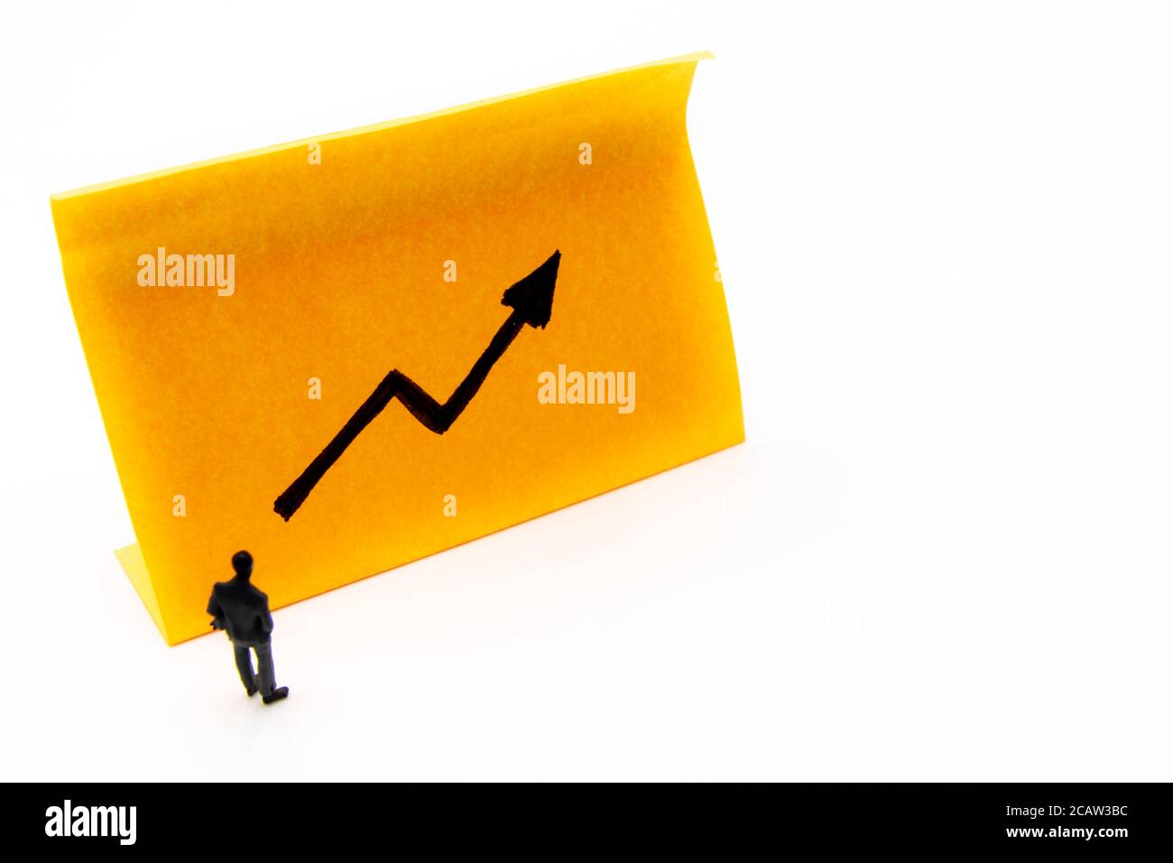 Miniature figurine posed as businessman in front of ascending graph arrow hand drawn on adhesive paper note, positive performance concept image Stock Photo
