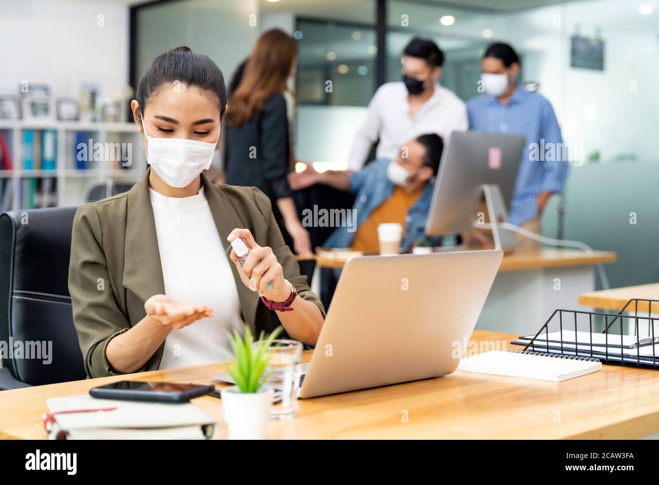 Asian office employee businesswoman wear protective face mask use alcohol spray hand sanitiser for hygiene in new normal office with social distance p Stock Photo