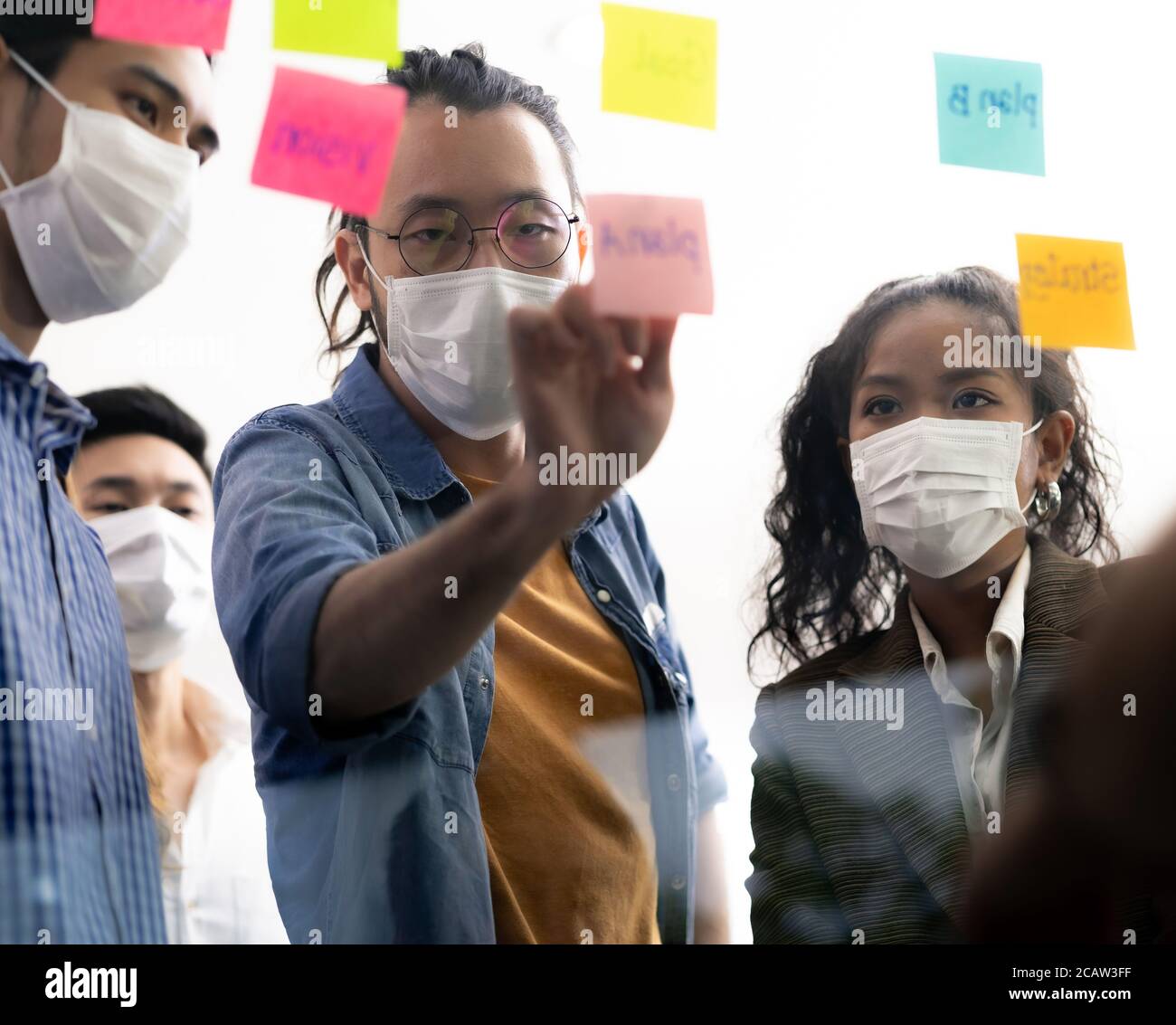 Interracial asian business team brainstorming idea at office meeting room after reopen due to coronavirus COVID-19 city lockdown. They wear face mask Stock Photo