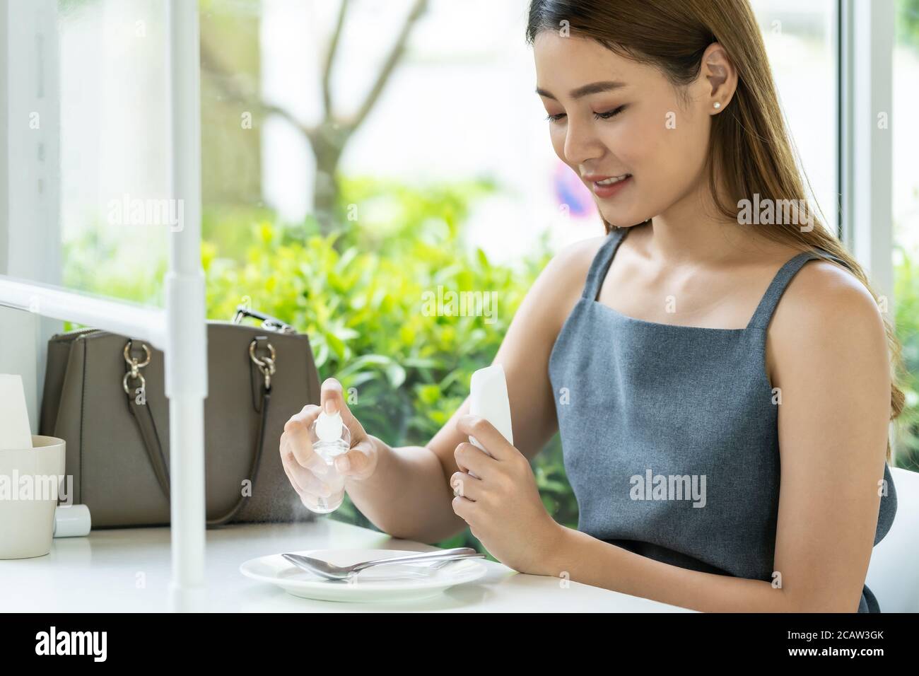 Asian attractive woman spraying alcohol on dish ware in restaurant to cleaning reduce infection of coronavirus covid-19. New normal lifestyle at resta Stock Photo