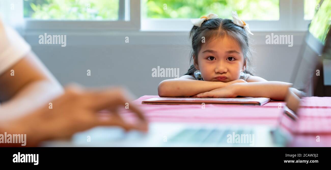 Asian upset girl looking and waiting her father working in dining room. Dad has to working from home while city lockdown from coronavirus covid-19 pan Stock Photo