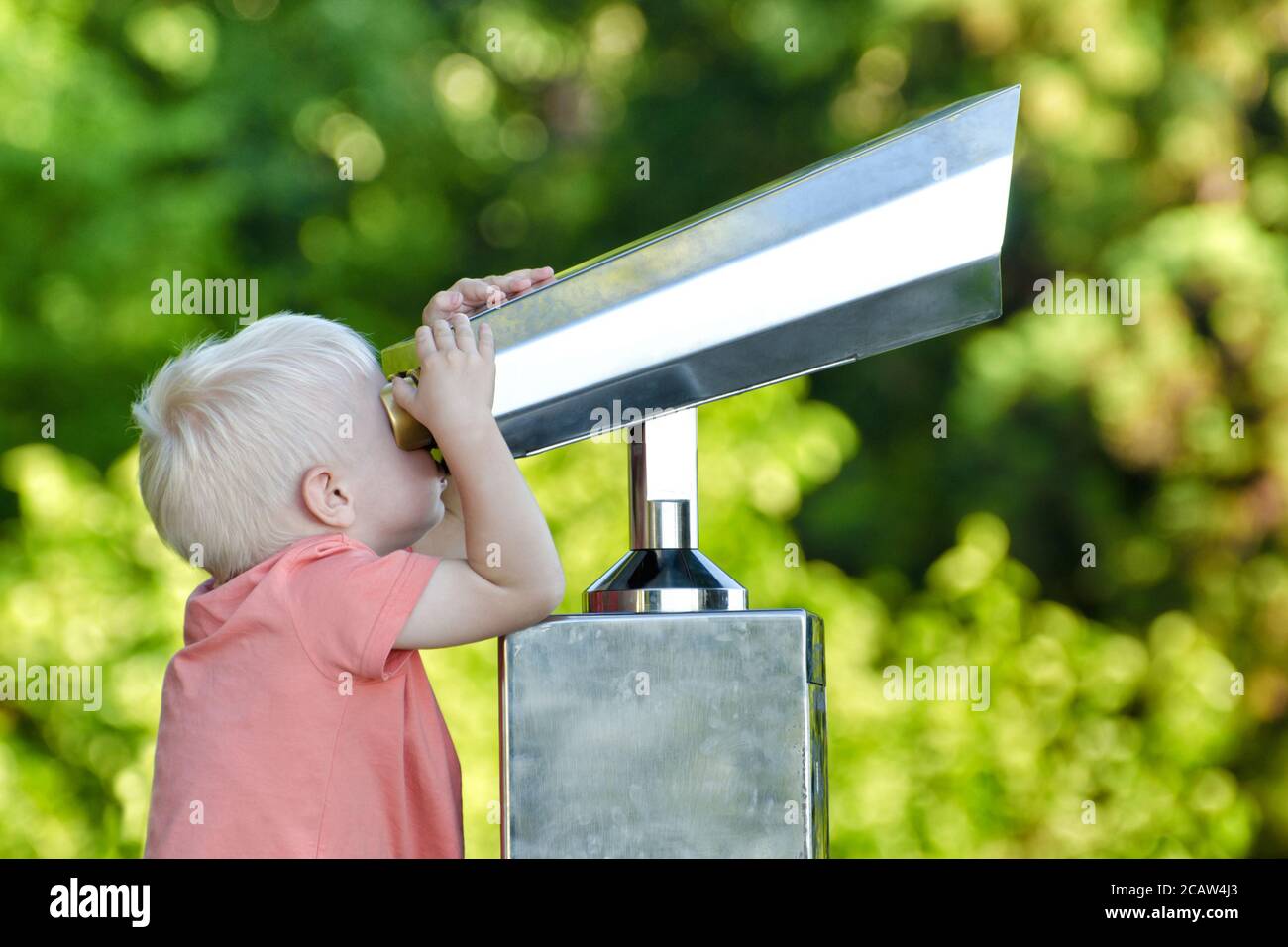 Little blond boy looking in a large pair of binoculars. Park in the background Stock Photo