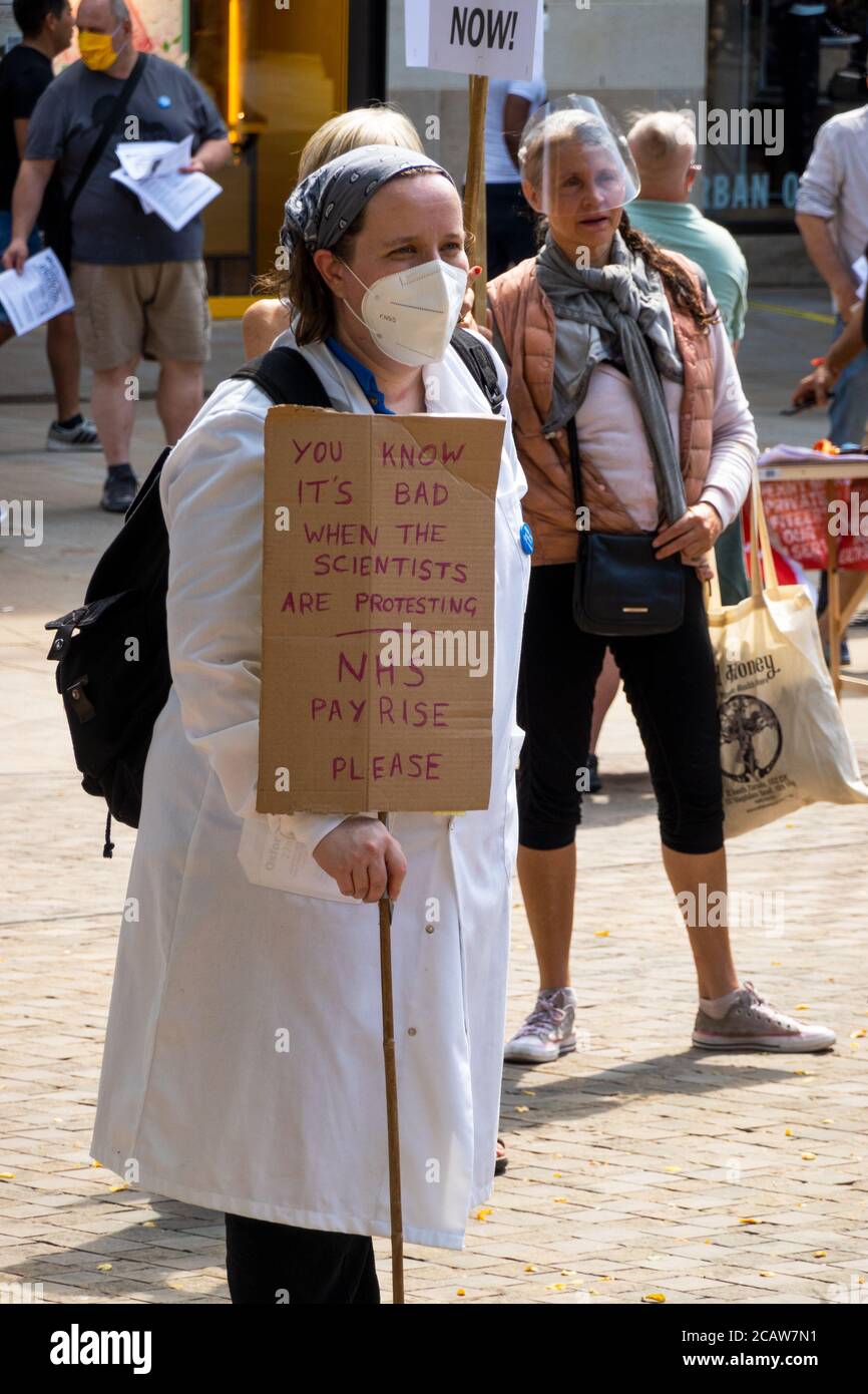 Oxford, UK. 8th August 2020. NHS workers and supporters attended a rally in Oxford’s Bonn Square calling for pay justice for all NHS workers, protesting to demand a pay rise to reflect their efforts during the covid pandemic This was one of around 38 similar rallies held throughout the UK. The protestors maintained social distancing and wore masks. While listening to speakers many held placards that highlighted their grievances and how they felt under valued. NHS worker wearing white lab coat with placard stating You Know It's Bad When The Scientists Are Protesting. Credit: Stephen Bell/Alamy Stock Photo