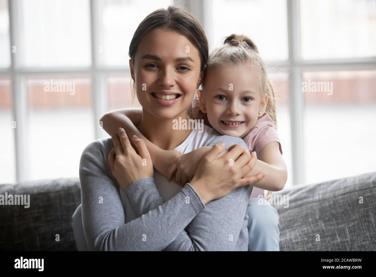 Cute little girl cuddling smiling beautiful young mother. Stock Photo
