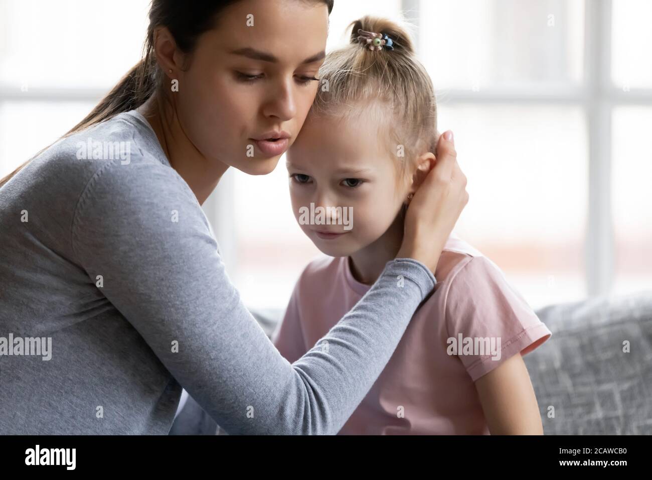 Worrying young mother comforting little stressed crying daughter. Stock Photo