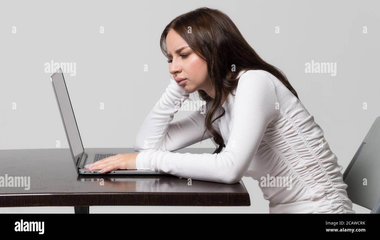Incorrect, impaired posture position, defect scoliosis, orthopedics concept. Young woman sitting at table, looking and working at laptop, isolated. Ra Stock Photo