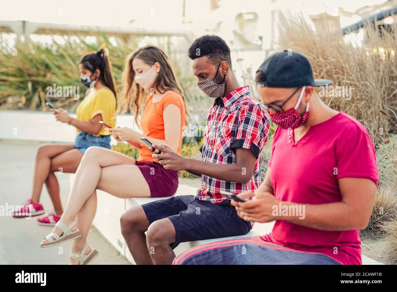Friends using their smartphones in covid 19 times protected with face mask - Young people using mobile device in distance outdoors Stock Photo
