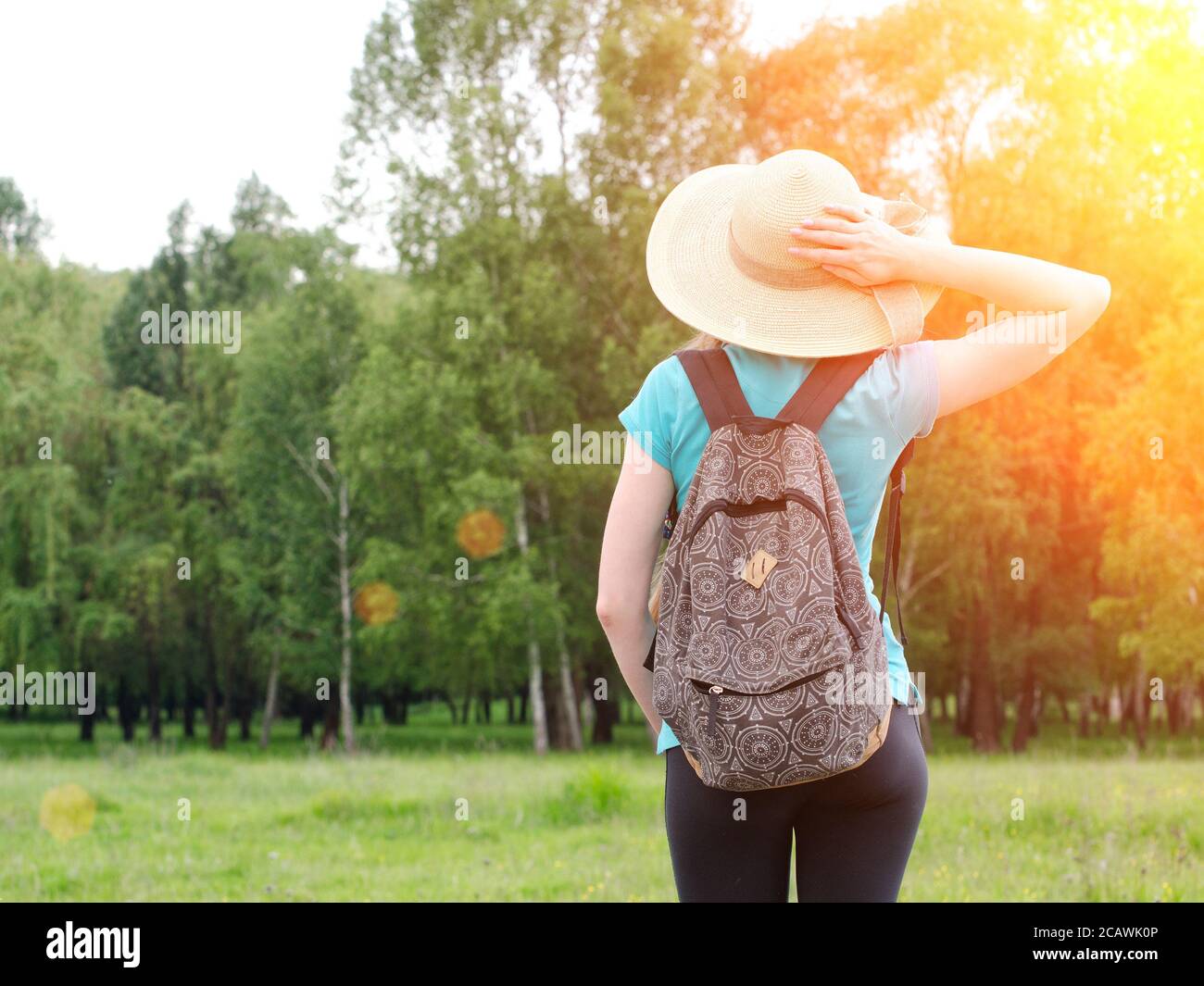Girl in hat and backpack holds hand behind the head on a background of