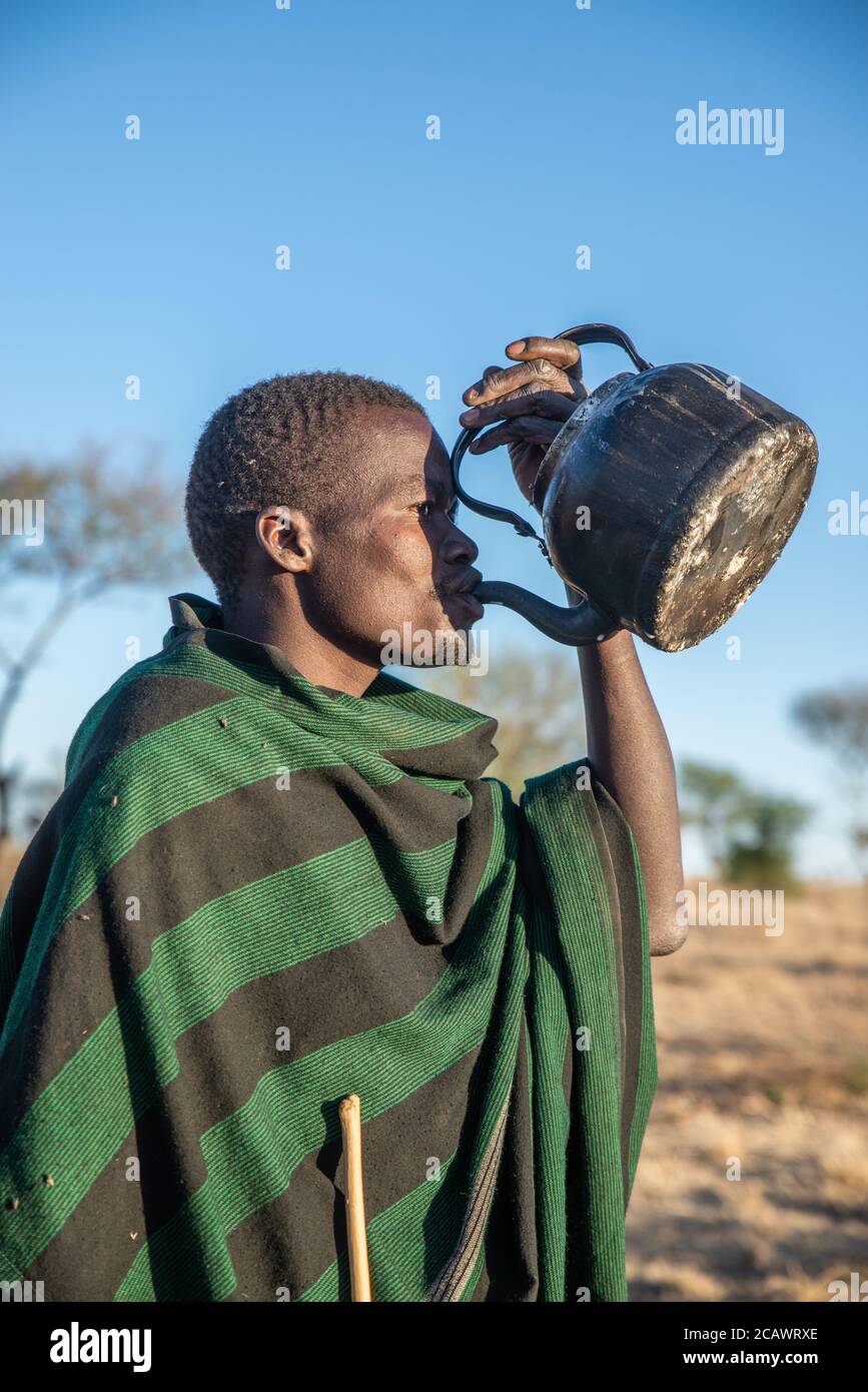 Karamojong cattle herder with traditional blanket drinking from a kettle, Moroto District, Uganda Stock Photo