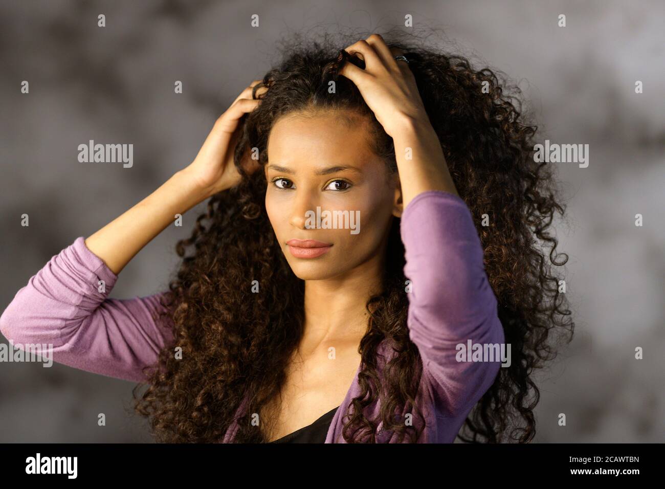 Cute attractive Afro American girl touching her long luxurious thick curly black hair with her hands as she turns to look at the camera Stock Photo