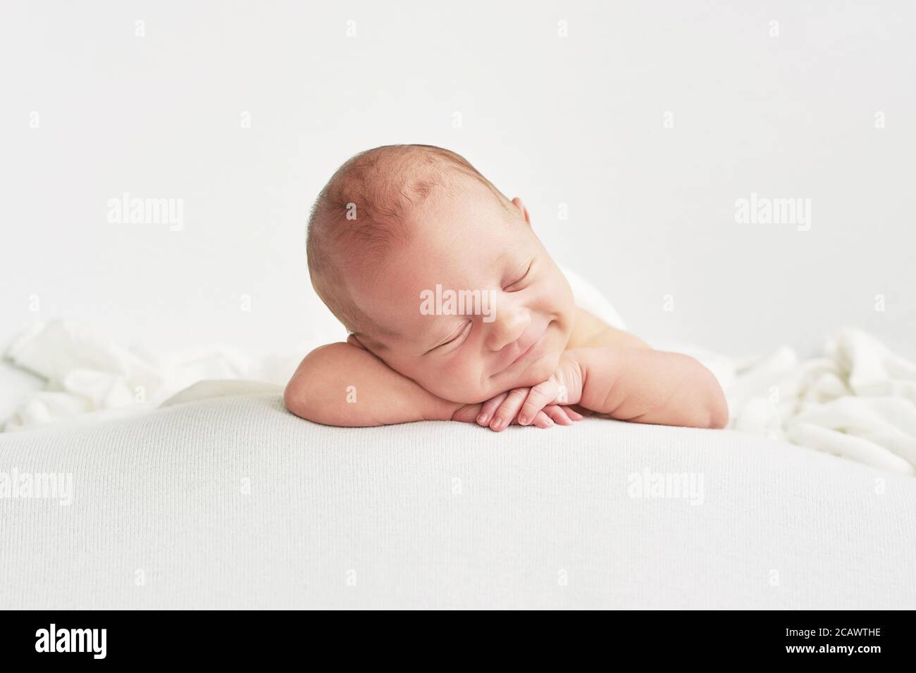 Cute newborn baby lies swaddled in a white blanket. Baby goods packaging template. Closeup portrait of newborn baby with smile on face. Stock Photo