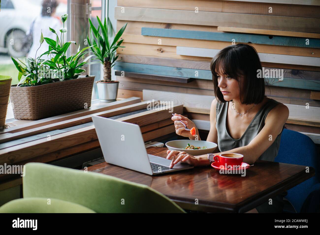Immersed woman eating vegeterian dish in a cafe while watching her laptop. Stock Photo