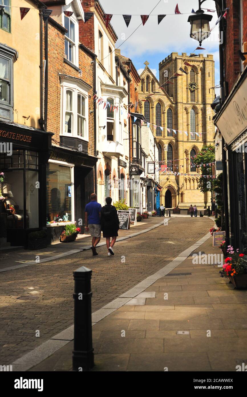 A couple strolls through the ancient City of Ripon, North Yorkshire, UK towards the Cathedral on a sunny afternoon Stock Photo