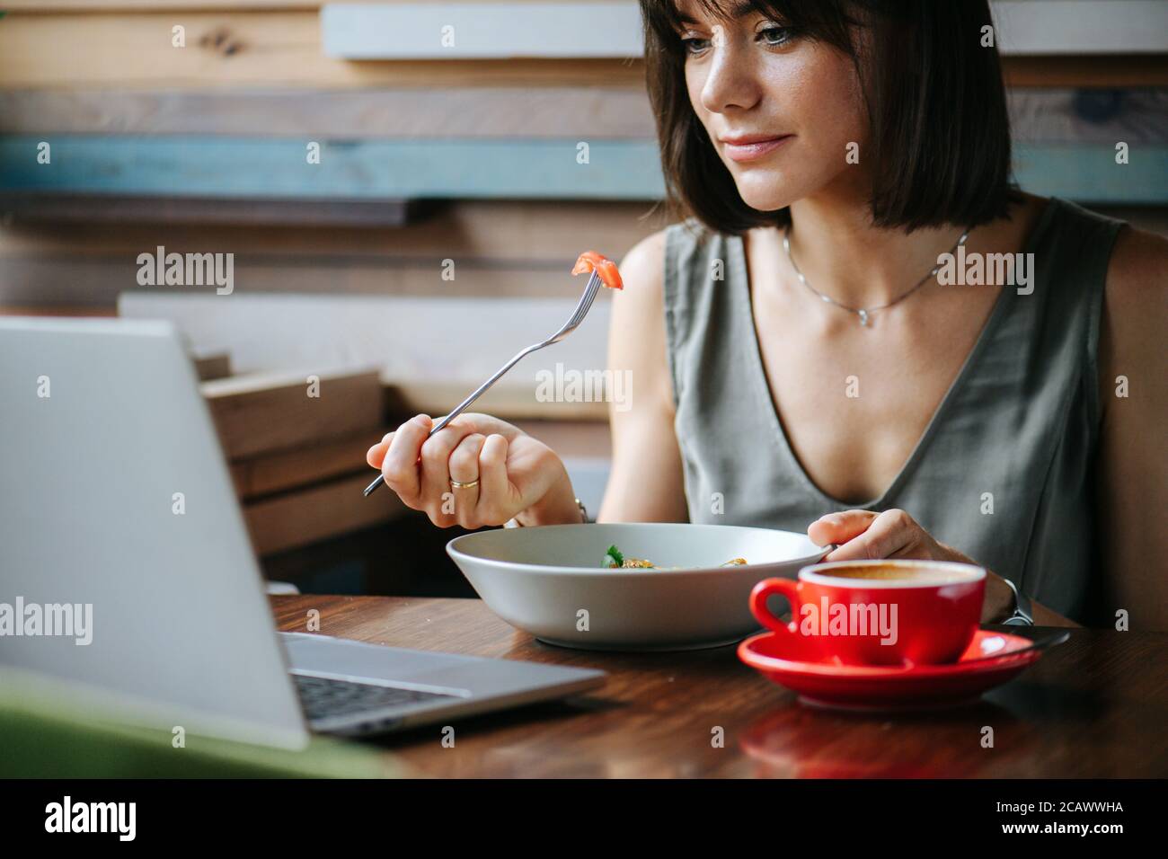 Woman enjoying herself, eating vegeterian dish in a cafe while watching laptop. Stock Photo