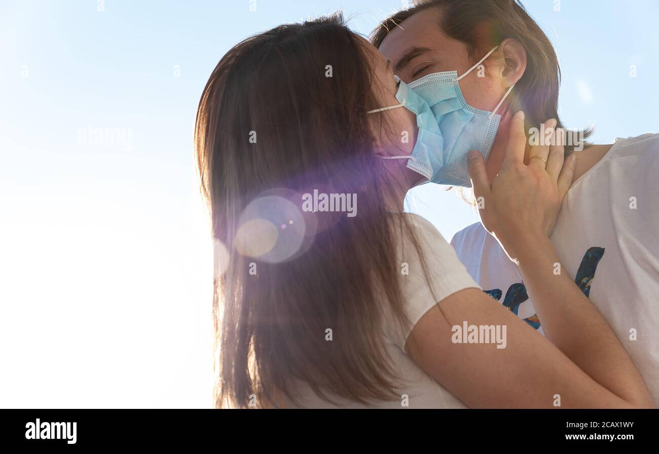 Young man and woman kissing with surgical face masks on, quarantine, Covid-19 protection. Love during coronavirus pandemic. Stock Photo