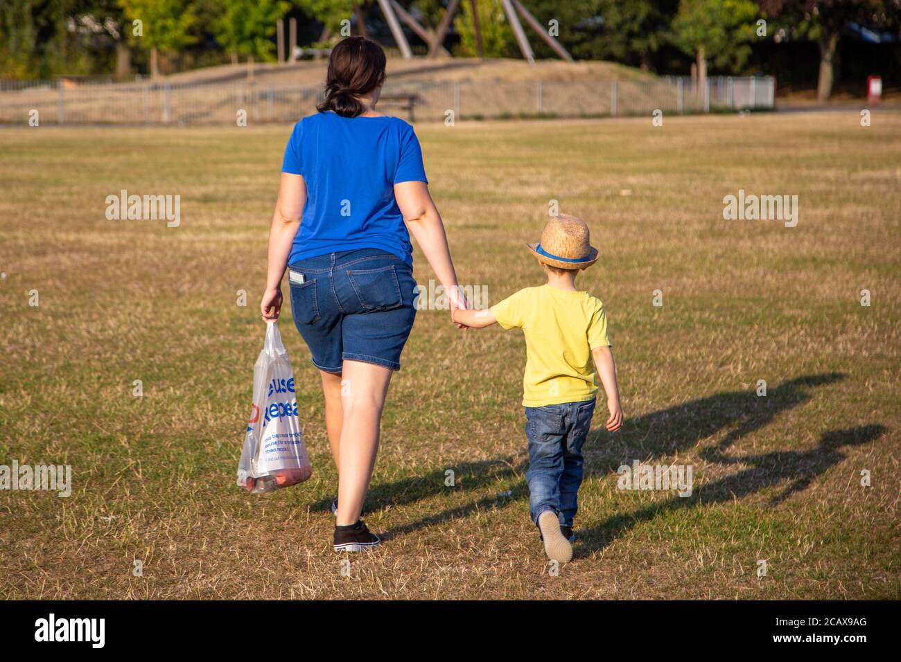A Mother and son walking through a park holding hands on a summers day Stock Photo