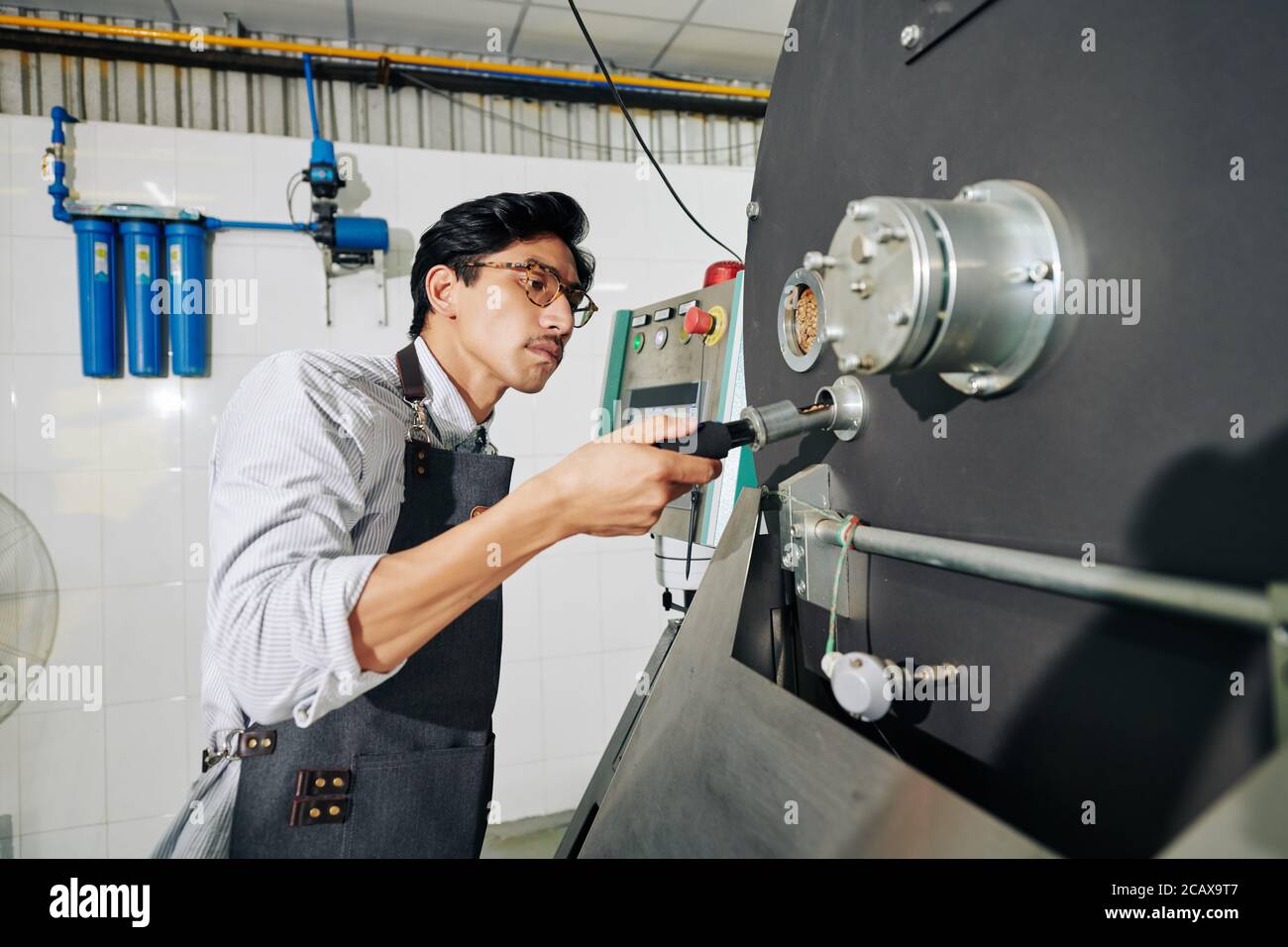 Serious Vietnamese roastery worker using probe when controlling roasting process Stock Photo