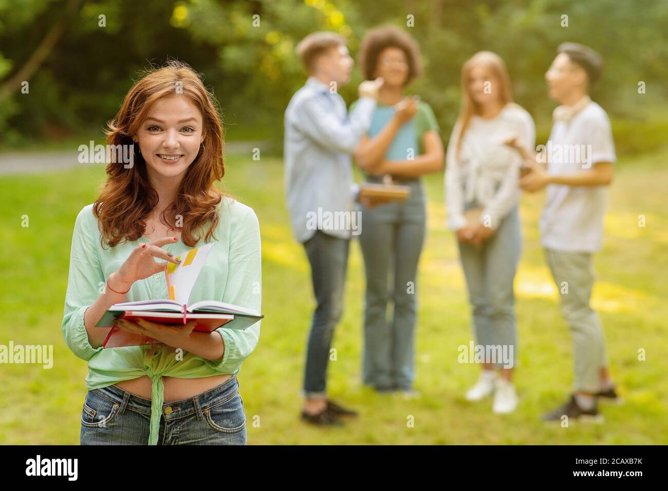 Portrait Of Smiling College Student Girl With Workbooks Posing Outdoors At Campus Stock Photo