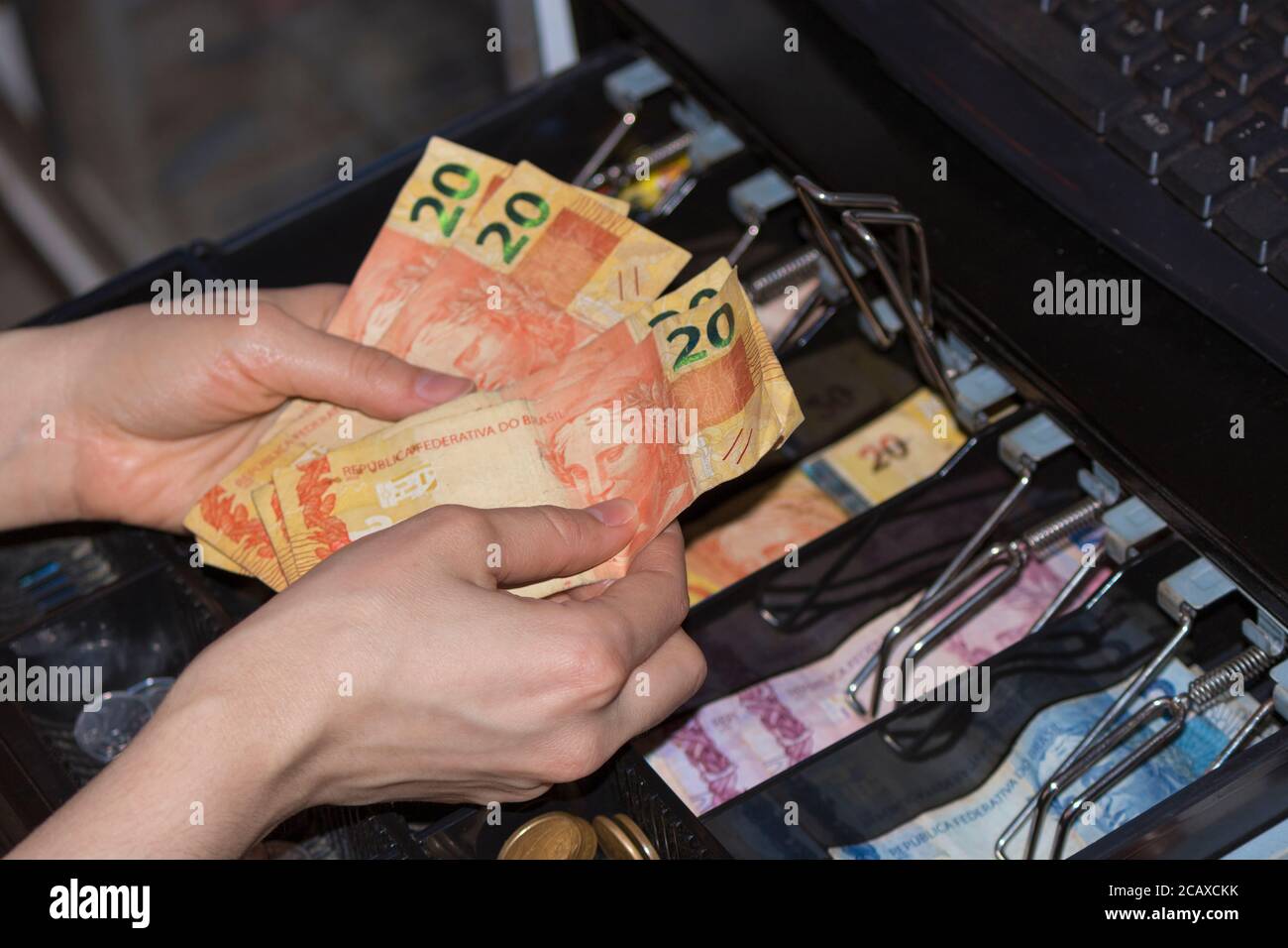 Saleswoman hands at cash register with brazilian money notes and coins inside the electronic cash register Stock Photo