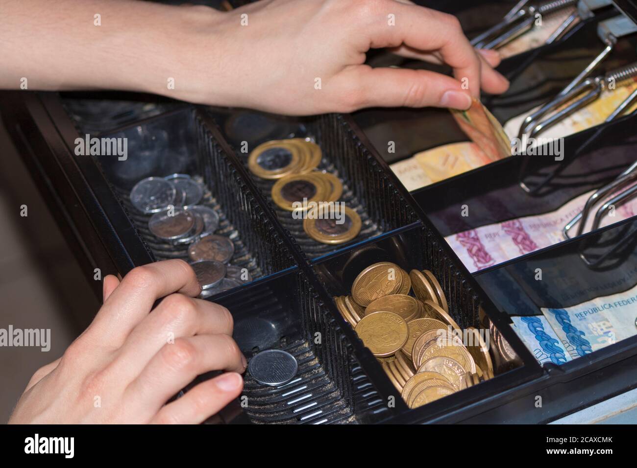 Saleswoman hands at cash register with brazilian money notes and coins inside the electronic cash register Stock Photo