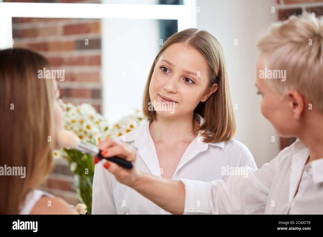 team of professional caucasian makeup artists working with young model. two make-up artist doing make-up in two hands and talk Stock Photo