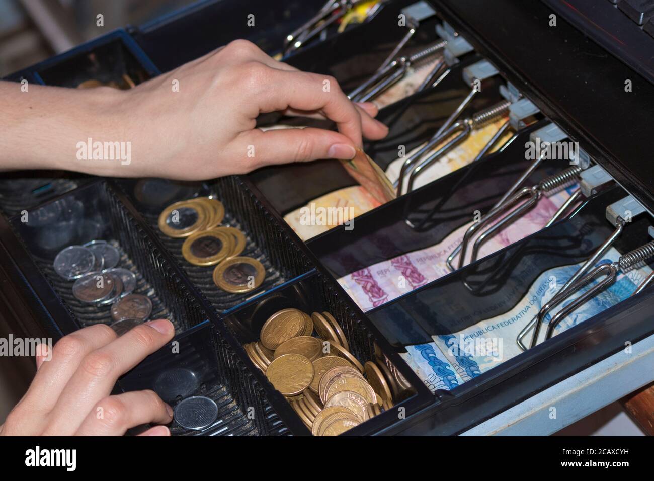 Saleswoman hands at cash register with brazilian money notes and coins inside the electronic cash register Stock Photo