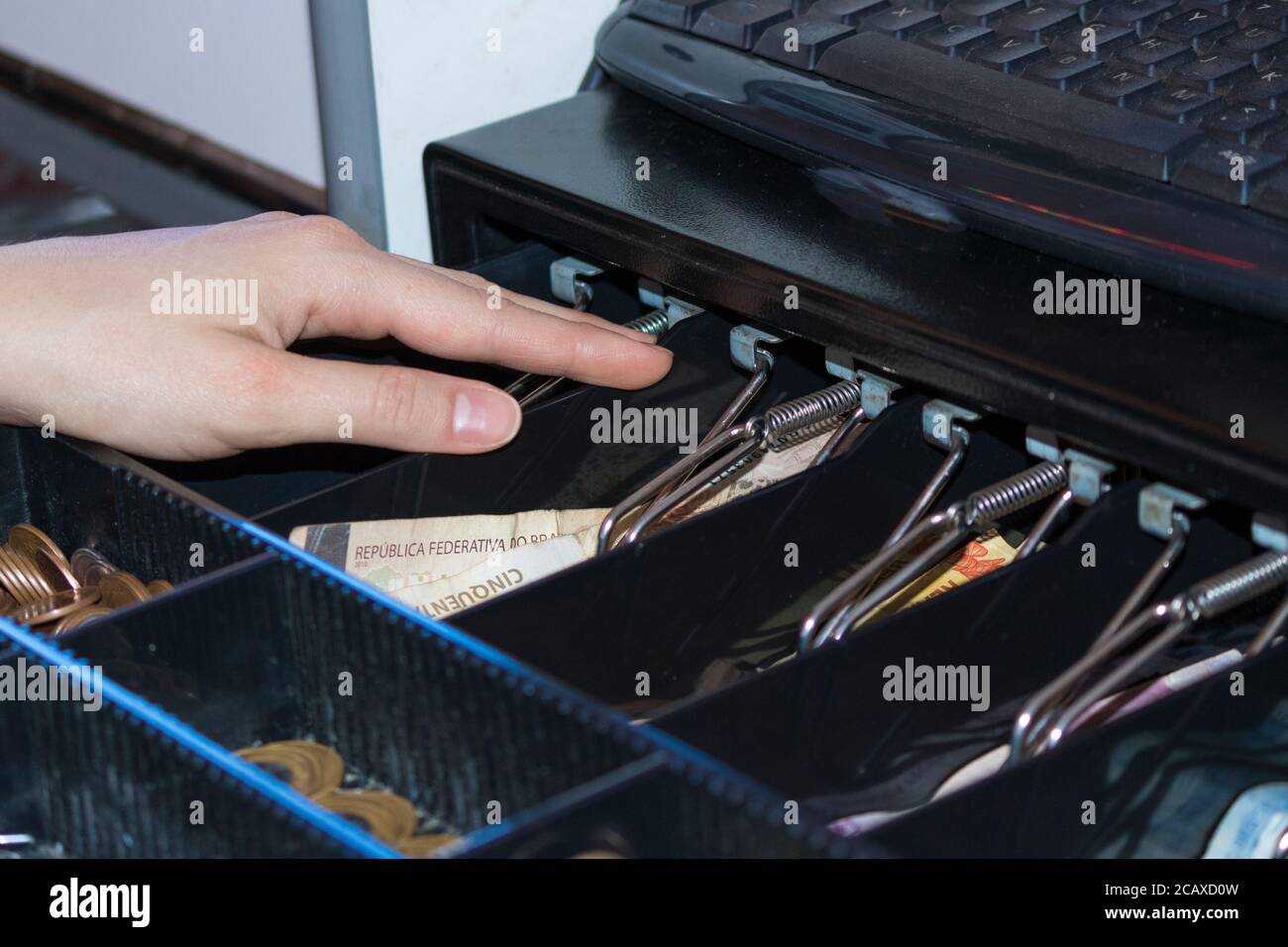 Saleswoman hands at cash register with brazilian money notes and coins inside the electronic cash register Stock Photo