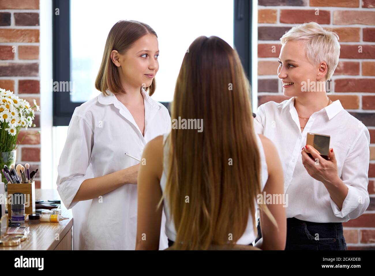 beautiful make-up artist and girls pupils discuss cosmetics on master class, professional visagist explain which of cosmetics for what is suitable for Stock Photo