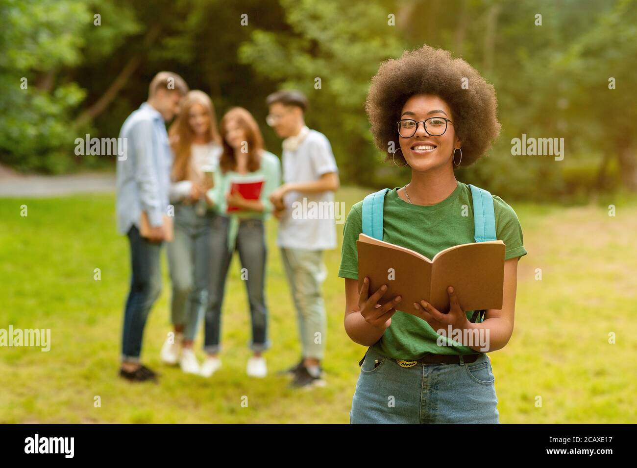 Smiling Nerd Black Girl Posing With Book Outdoors At Campus Stock Photo