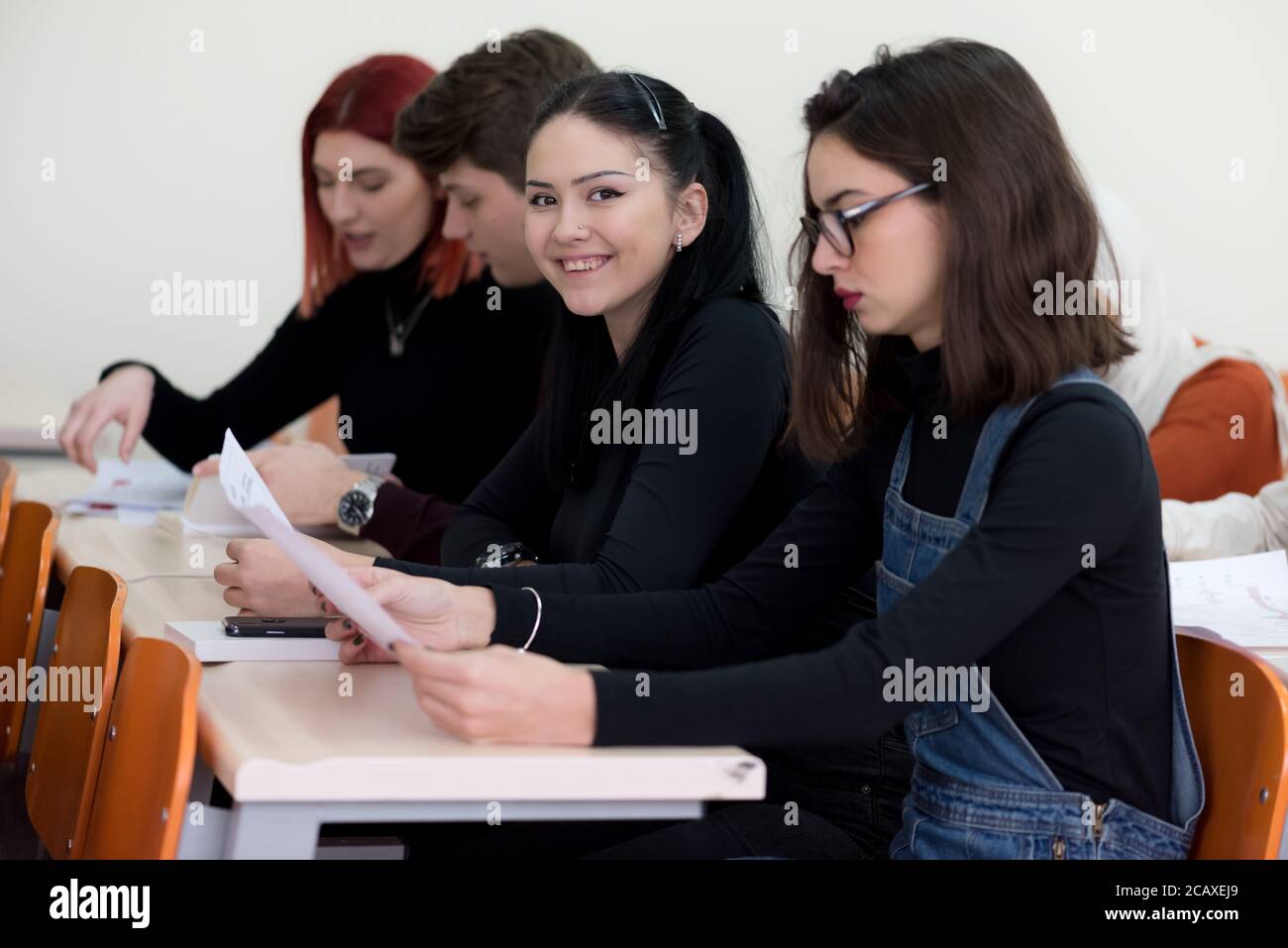 Exams Preparation. Group Of Multi-Ethnic Students Studying Together inside classroom while helping each other. Female student smiling into camera. Stock Photo