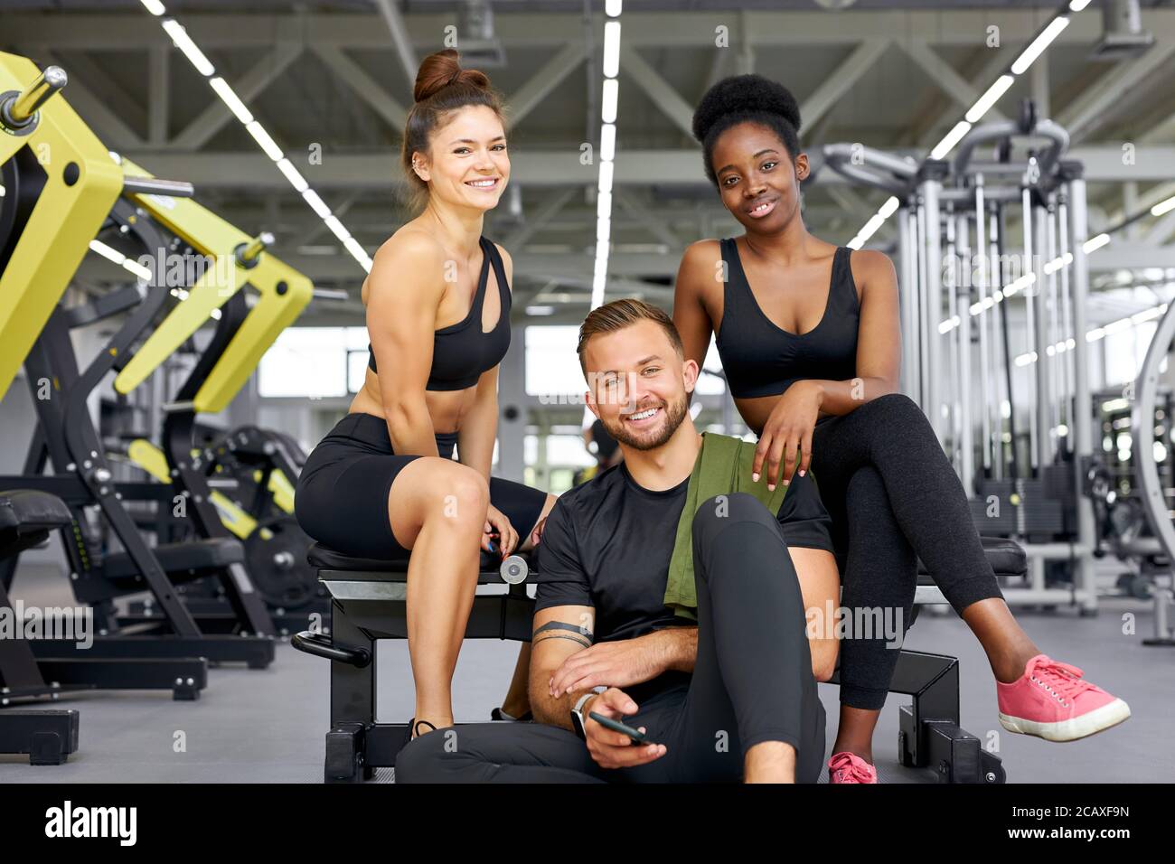 two fit girls training with personal trainer in gym, attractive african and  caucasian women with strong male have rest after exercises Stock Photo -  Alamy