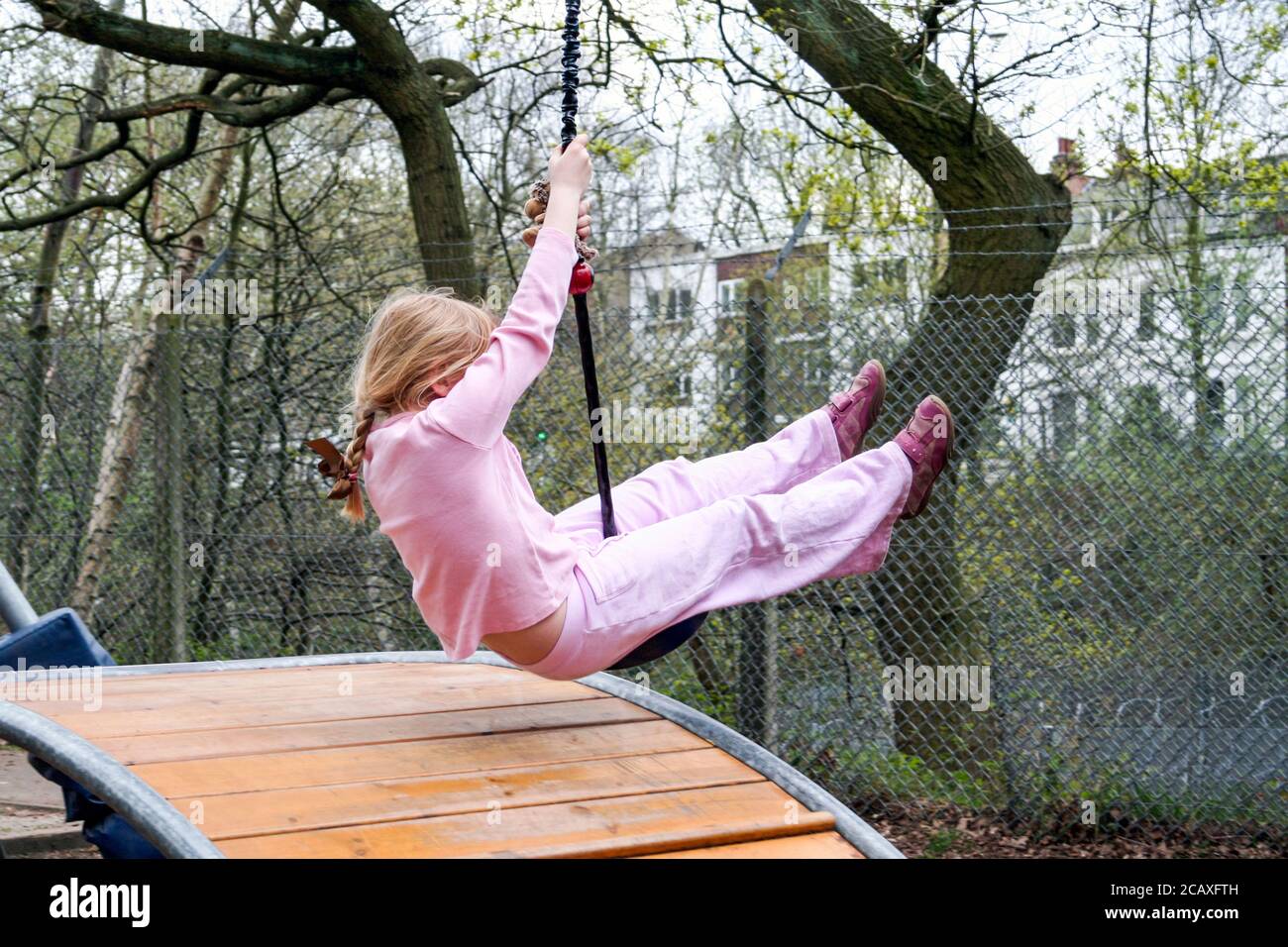 A 6-7 year old girl dressed in pink on a zip wire in a playground, London, UK Stock Photo