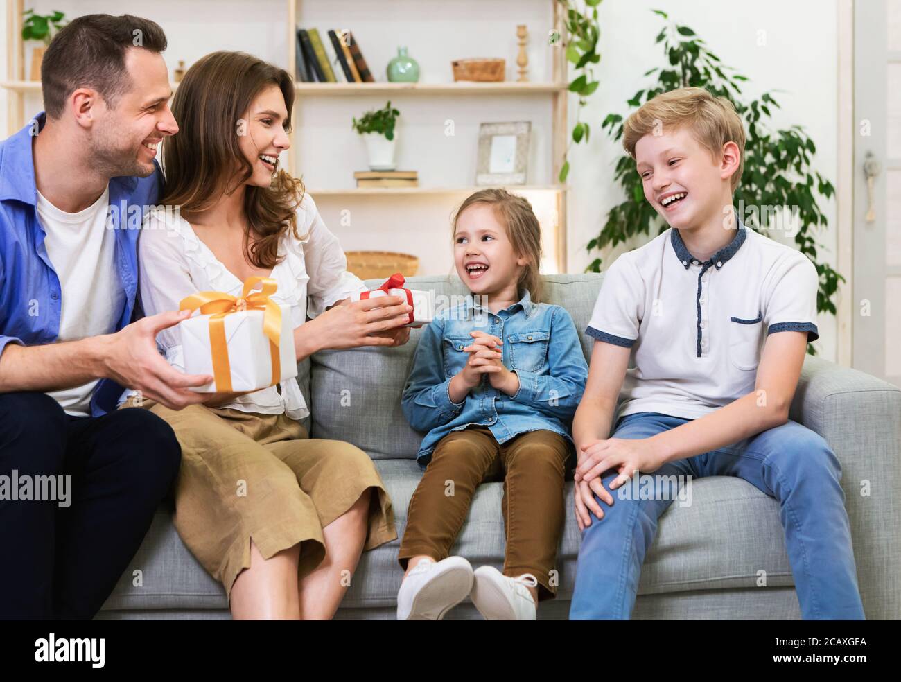Happy Parents Giving Gifts To Kids Celebrating Holiday Sitting Indoors Stock Photo