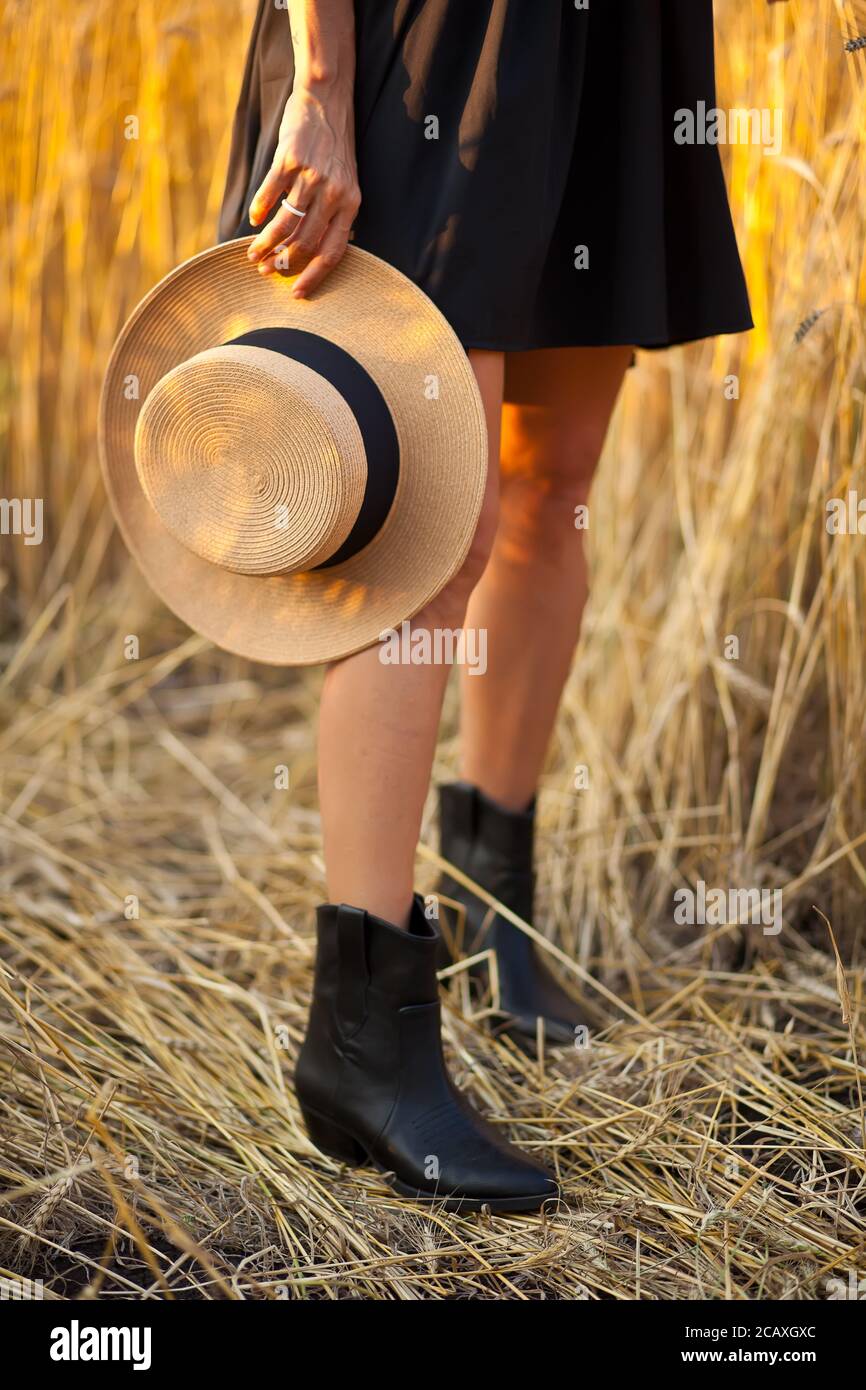 Young woman in black dress standing in field with wheat and holding a ...