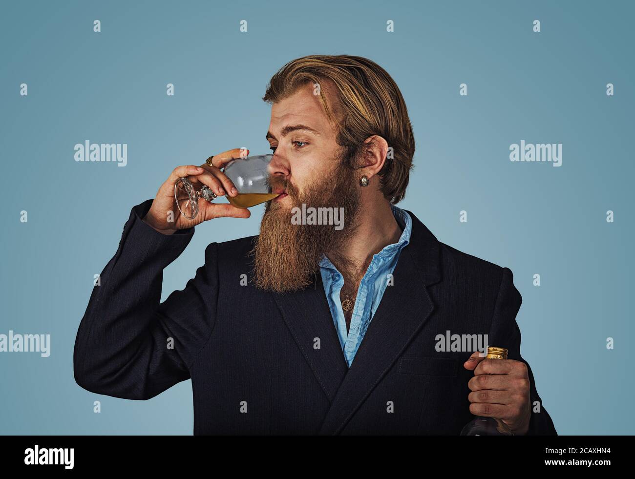 Handsome bearded well-dressed man in jacket holding tasting drinking glass of beverage whiskey alcohol isolated on grey gray studio background wall. d Stock Photo