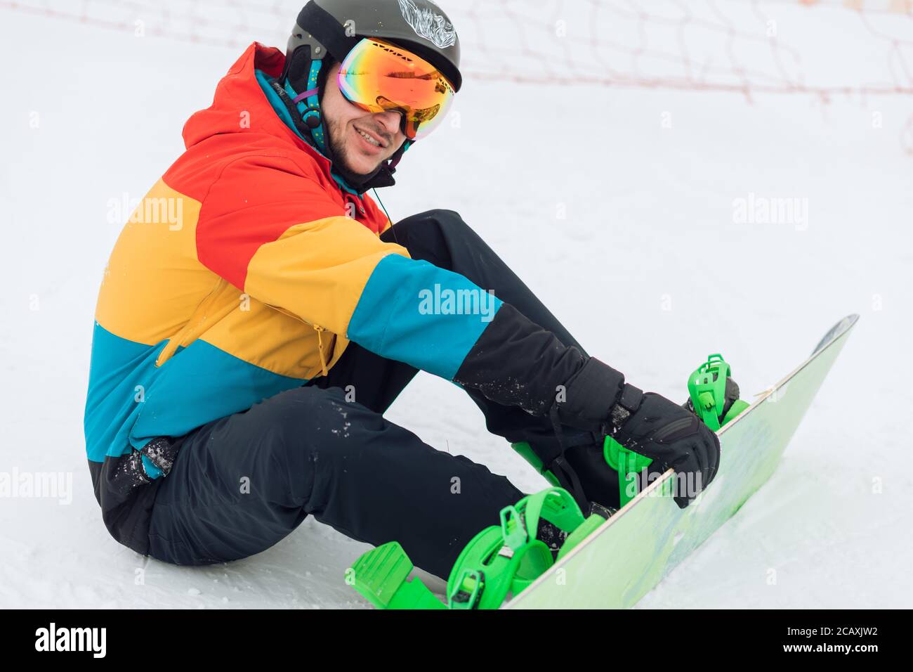 close up side view photo. Snowboarder sitting on snow and checking his equipment Stock Photo