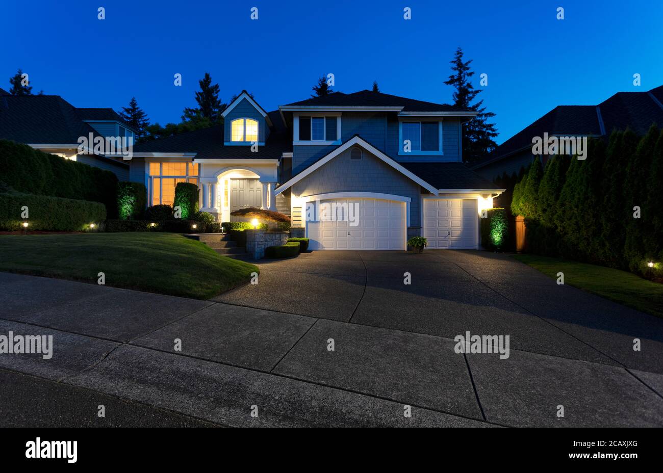 Modern suburban home exterior on a late summer evening with lights on yard and house Stock Photo