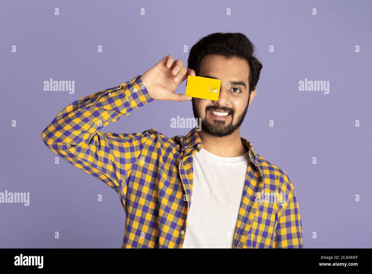 Positive Indian guy closing eye with contactless credit card on violet ...