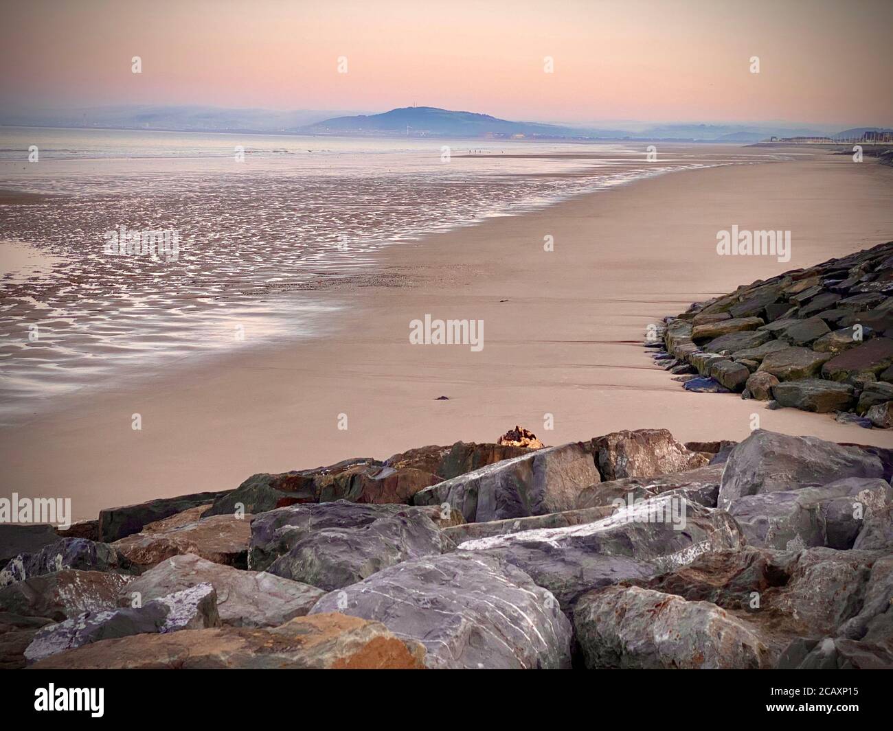 Idyllic empty beach seashore scene at sunrise, showing rocks, sand, sea and hills in the background Stock Photo