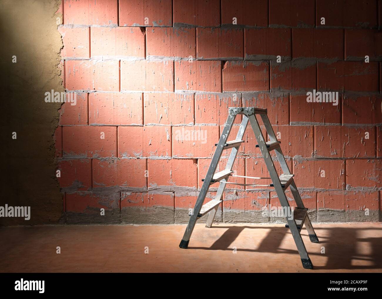 Step ladder in front of a brick wall from Porotherm style blocks partly plastered with clay in a construction site of a new building, copy space Stock Photo