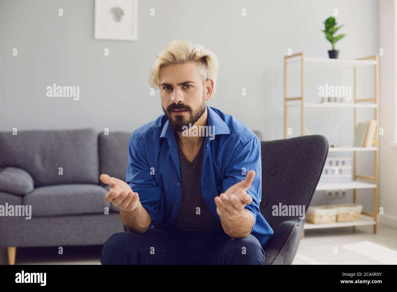 Confused hipster man sitting in armchair at home Stock Photo