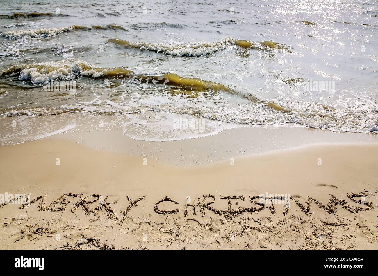 “Merry Christmas” is written in the sand on the beach as waves crash, Dec. 24, 2012, in Dauphin Island, Alabama. Stock Photo