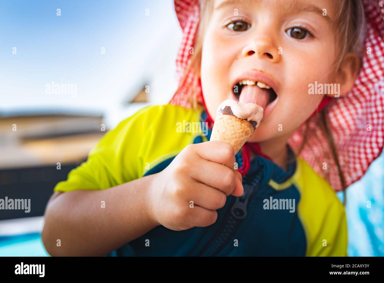 Portrait little child with big eyes licking icecream in summer. 2 year old baby girl. Stock Photo