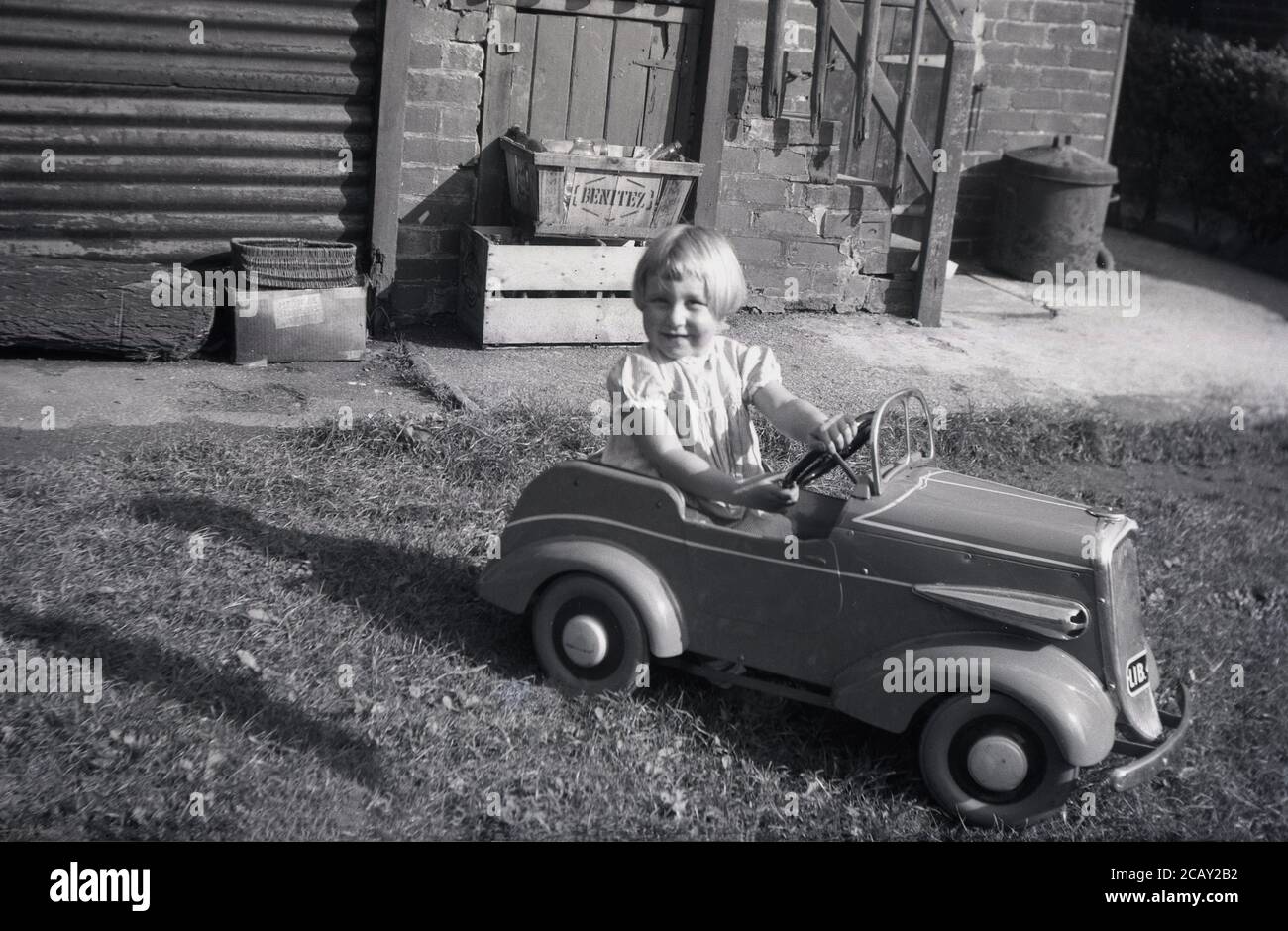 1940s, historical, outside in a back yard or garden, a little girl sitting in her ride on toy car on some grass. Stock Photo
