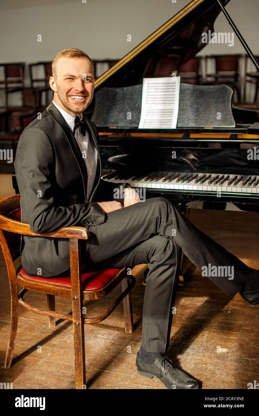 good-looking caucasian male pianist sit, look at camera and smile. professional classical music performer before performance on a stage Stock Photo