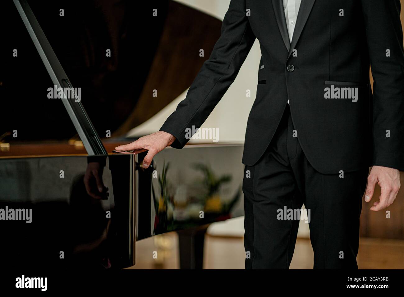 portrait of young caucasian man in formal elegant suit standing next to piano, professional musician after performance Stock Photo