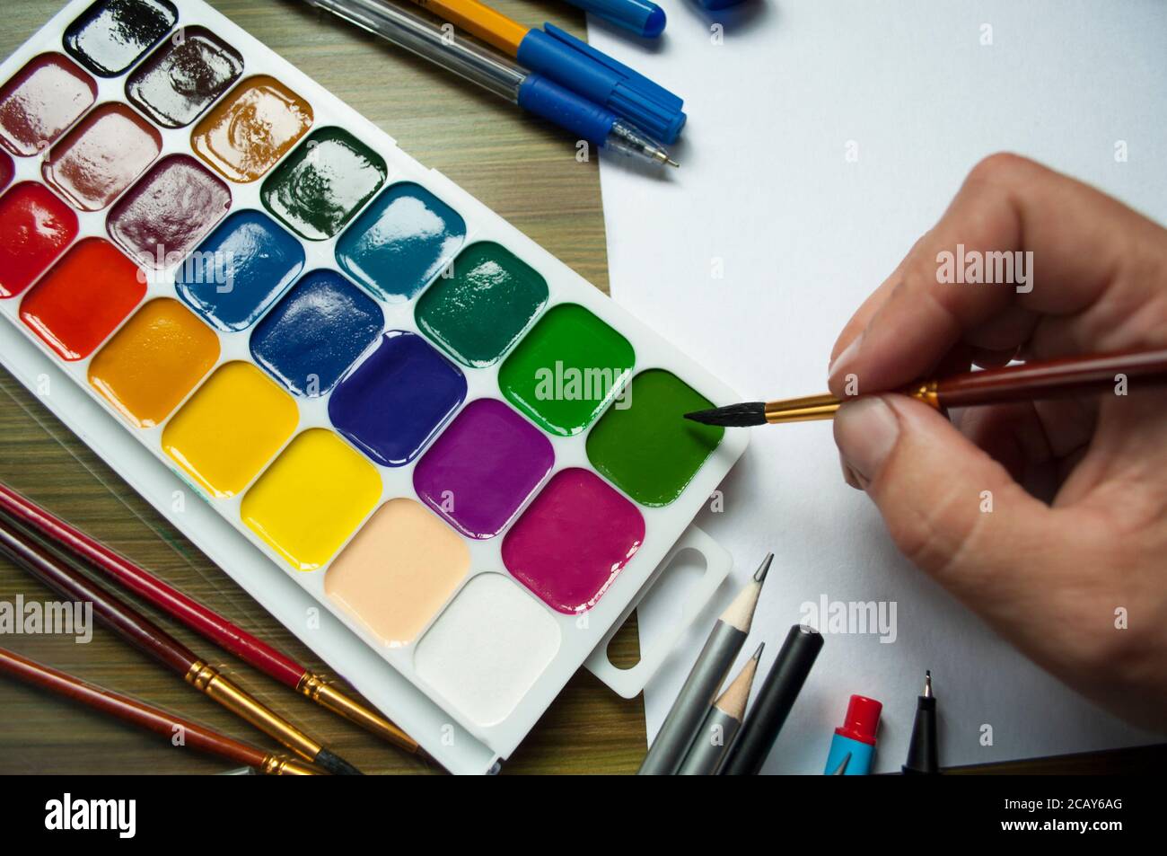 Female hand shakes the brush and soaks in watercolor paints. The photo  shows pencils, brushes, paints, pens and white paper Stock Photo - Alamy
