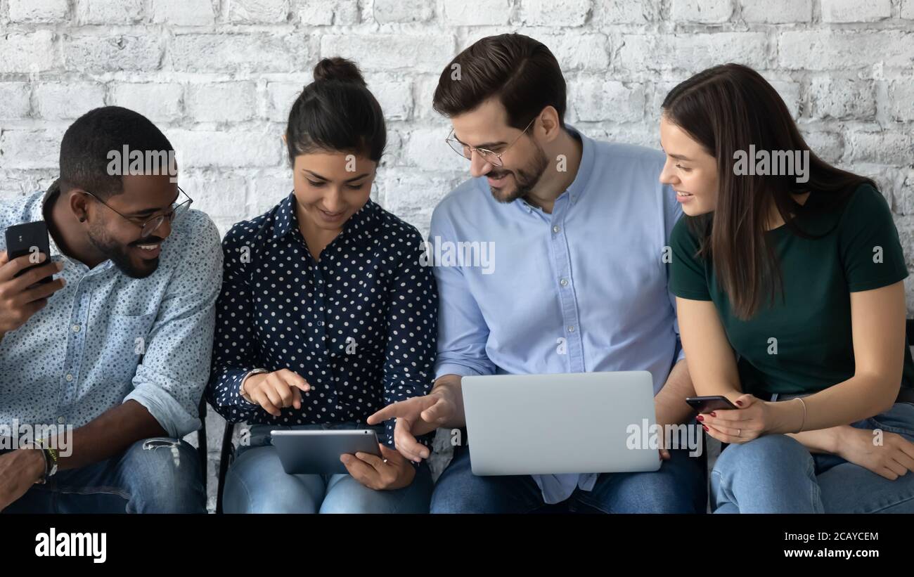 Friendly diverse candidates talking, using mobile devices, waiting for interview Stock Photo